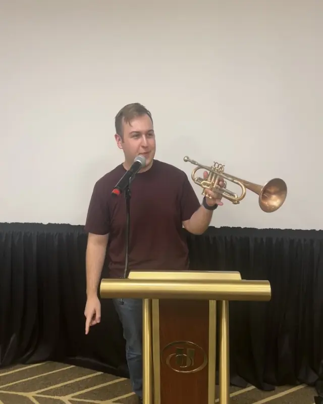 Harrisson Ball at a podium microphone, holding up his trumpet