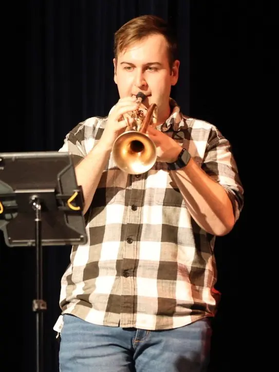 Harrisson Ball playing trumpet on a dark stage with a tablet on the music stand