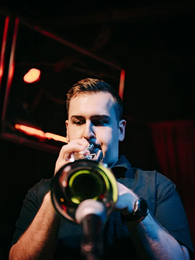 Harrisson Ball playing trumpet on stage under red light, bell toward the camera