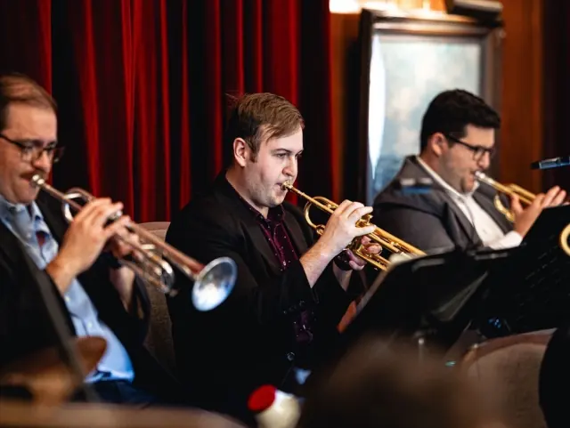Harrisson Ball playing lead trumpet in a three-trumpet section in front of red curtains