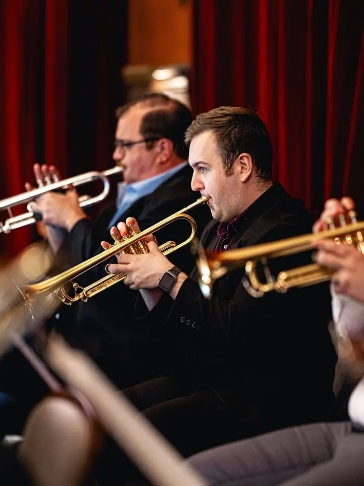 Harrisson Ball in profile playing trumpet in a big band section in front of red curtains
