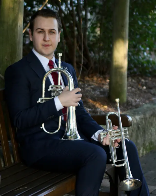 Press portrait of Harrisson Ball on a park bench holding a flugelhorn and a trumpet