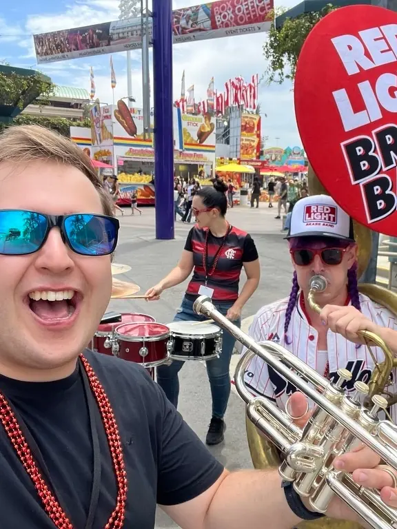 Harrisson Ball in sunglasses with a silver trumpet in front of a Red Light Brass Band sign