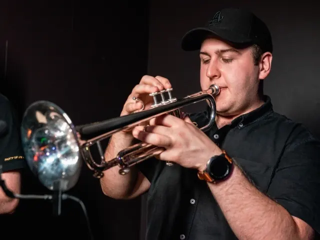 Harrisson Ball in a black cap playing a silver trumpet into a stage microphone