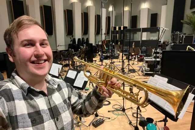 Harrisson Ball smiling with his gold trumpet on a big scoring stage full of microphone stands