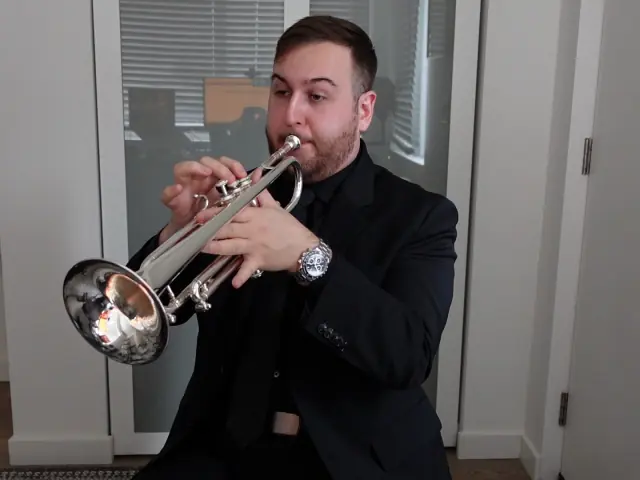 Harrisson Ball in a black suit playing a silver trumpet in a white room